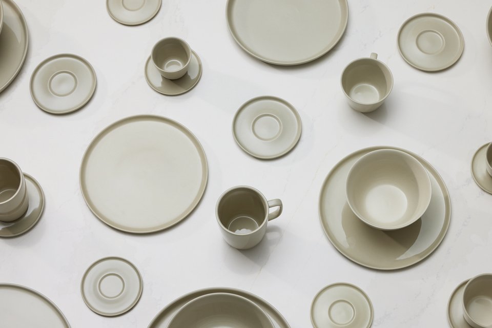 Multiple grey coloured plates, cups and saucers on top of a white table.